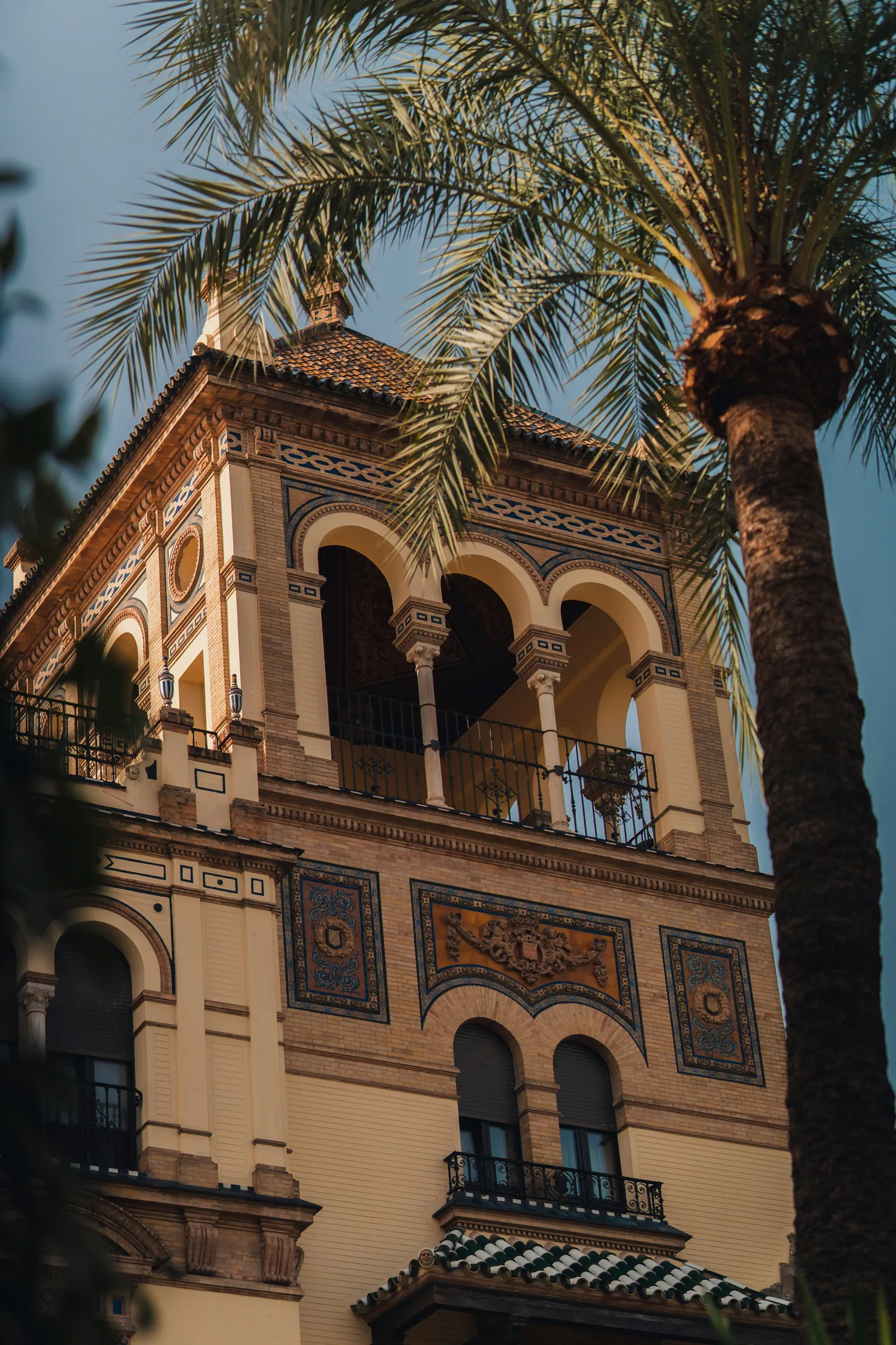 Turm mit Bögen und Azulejos hinter einer Palme in Sevilla